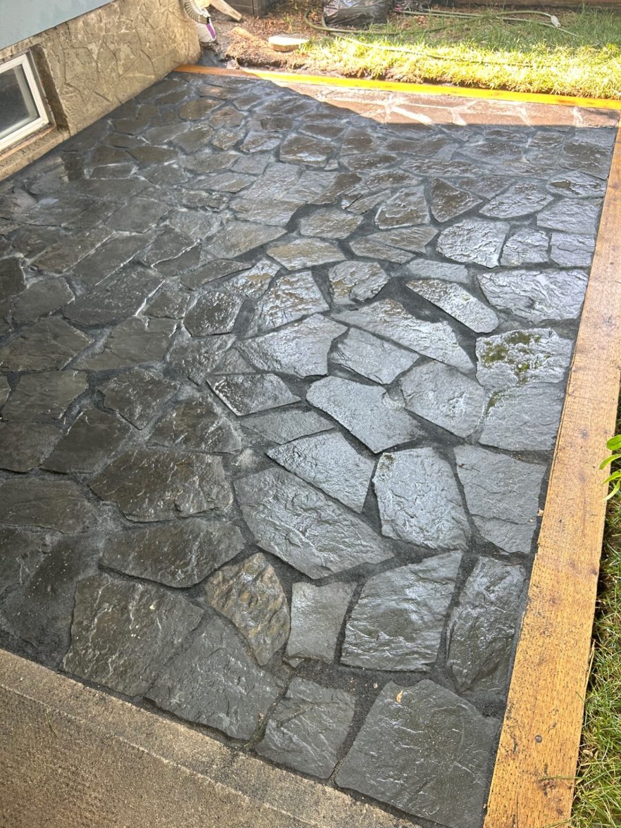 Flagstone 001 Stamped concrete patio with dark stone texture beside home foundation.